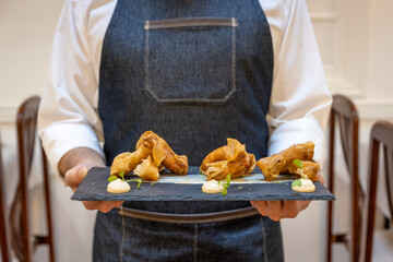 Waiter holding a fancy meal on a black plate in the restaurant