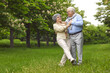 © Studio Romantic - Senior man and woman are dancing on the green grass in the park among the trees. A man holds a woman, wear glasses, and a scarf, happy family life. Walk in the fresh air.