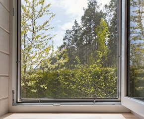 White window with mosuito net in a rustic wooden house overlooking the blossom garden.