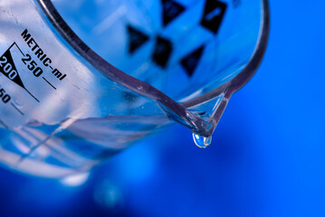 Canvas Print - Macro shot of a water drop falling from a glass jug with blurred light background