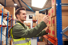 Male Worker Wearing Inside Warehouse Scanning Stock Barcode On Shelves Using Digital Device Or Phone