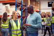 © Monkey Business - Female Intern With Team Leader Looking At Digital Tablet Inside Busy Warehouse Facility