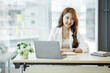 © David - Portrait of Asian young businesswoman with laptop writes on a document at her office,Asian girl working at a office space with a laptop computer.