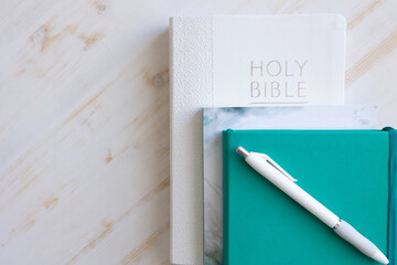 White Christian bible with teal journal and white pen and devotional on a white wood background with copy space