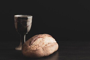 Wall Mural - Loaf of bread and clay chalice on a black background with copy space