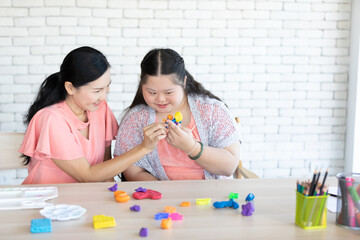 Wall Mural - down syndrome girl with woman teacher learning to use colorful and play dough on a table