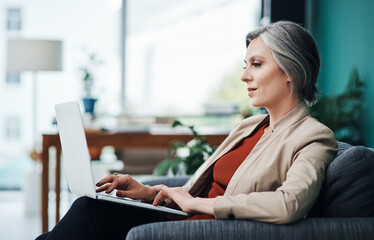 Wall Mural - Responding to emails. Cropped shot of an attractive mature businesswoman sitting alone and using a laptop in her home office.