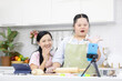 mother and down syndrome teenage girl or her daughter rolling out dough and live streaming online via smartphone on tripod in a kitchen