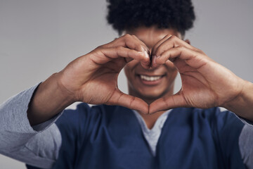 We dont just think with our heads, we think with our hearts. Shot of a male nurse forming a heart shape with his hands while standing against a grey background.