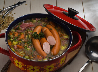 Traditional German Lentil soup with sausages, Linsensuppe in a red cooking pot on a wooden table