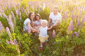 Wall Mural - Happy family mother father embracing kids outdoor. Woman man baby child and teenage girl sitting on summer field with blooming flowers background. Happy family mom dad and daughters playing on meadow.