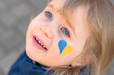 Fototapeta  - portrait of a girl with a blue and yellow heart on the cheek 