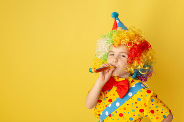 Wall Mural - Funny kid clown against yellow background. Happy child playing with festive decor. Birthday and 1 April Fool's day concept