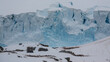 Atemberaubend und wild, eine Kolonie von Pinguinen errichtet auf einem Felsplateau Nester für die Brut, im Hintergrund türmen sich riesige blaue Gletscherwände auf