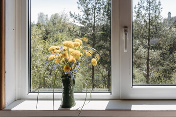 bouquet of yellow dandelions in clay vase standing on windowsill by open window in countryside