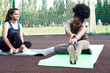 © etonastenka - Two lovely young women stretch while sitting on yoga mats before training outdoors. Girlfriends go in for sports at the stadium