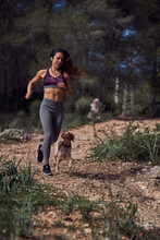 Active Young Hispanic Sportswoman With Dog Running Along Rough Path In Woods