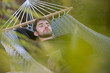 Jeune homme de 20 ans qui fait la sieste dans son jardin, allongé dans un hamac. Au premier plan, il y a des plantes.