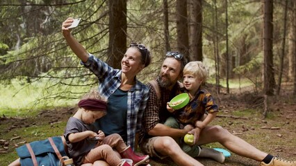 Wall Mural - Family with small children having picnic in summer forest and taking selfie.