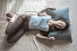 Young happy woman is lying in bed in the morning with her eyes closed and waking up. Concept of healthy sleep, comfort and a pleasant start of new day. Top view