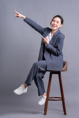 Wall Mural - Young Asian businesswoman sitting on chair and posing on gray background