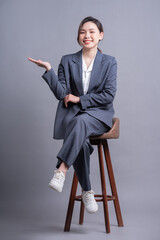 Wall Mural - Young Asian businesswoman sitting on chair and posing on gray background