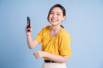 Wall Mural - Young Asian girl using smartphone on blue background