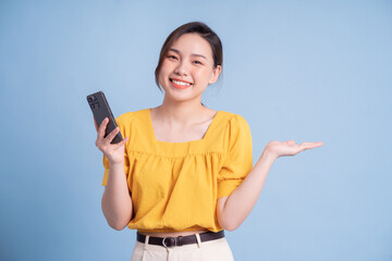 Wall Mural - Young Asian girl using smartphone on blue background