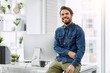© Nola V/peopleimages.com - The moment when the office is the best place to be. Cropped portrait of a handsome young businessman smiling while sitting on his desk in a modern office.