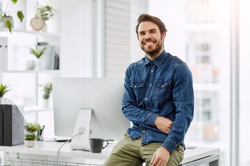 The moment when the office is the best place to be. Cropped portrait of a handsome young businessman smiling while sitting on his desk in a modern office.