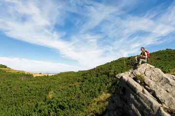 Poster - Young woman with backpack on rocky cliff in mountains