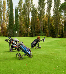 Golf cart with bag and golf clubs in the fairway of a golf course, parked at the edge of the green. In the background the green with the flag.