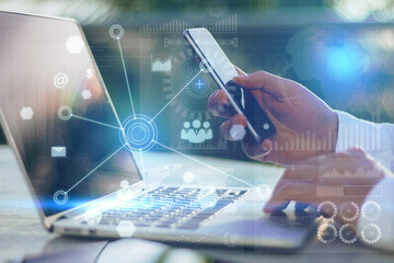 Poster - Close up of hand using laptop and smartphone with abstract global digital business interface on blurry background. Interface, chart and hud concept. Double exposure.