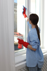 Canvas Print - Young woman cleaning window glass with rag and detergent at home, back view