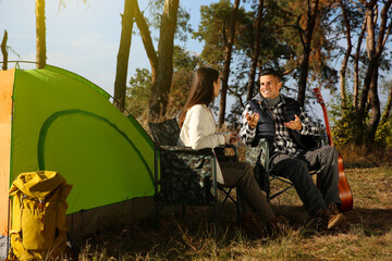 Wall Mural - Couple resting in camping chairs near tent outdoors