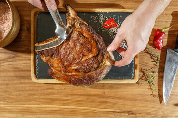 Wall Mural - the cook puts the Wet-Aged Steaks on a black plate with spices, prepares the serving of the steak