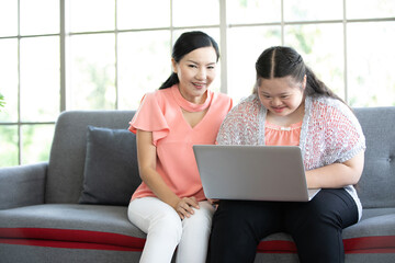 Wall Mural - mother using laptop computer and a girl with down syndrome or her daughter, smiling and enjoying on sofa