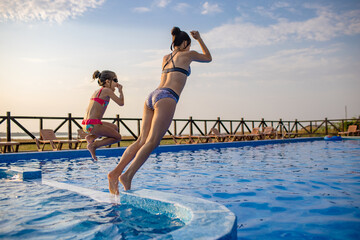 Canvas Print - Two girls jumping into the pool on summer vacation at sunset