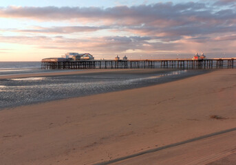 Wall Mural - the sun setting over the historic north pier in blackpool with glowing light reflected on the beach and colourful twilight sky