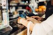 © Anna - Cropped of woman's hands holding paper coffee cup on bar counter at coffee shop. Woman ordering in restaurant and drinking coffee.