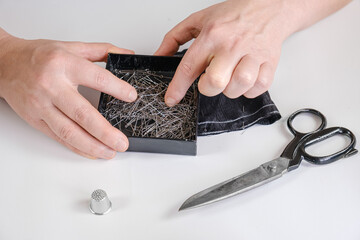 Wall Mural - The seamstress sorts out metal sewing pins. Close-up of female hands.