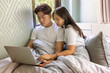 © Supavadee - couple working together with laptop on bed for a bedroom at home.