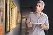 © JackF - Adult man is visiting museum with information brochure and looking at the pictures in the gallery indoor.
