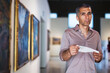 © JackF - Adult man is visiting museum with information brochure and looking at the pictures in the gallery indoor.