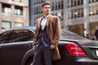 Young successful businessman walking to the office out of his car parked in a business center