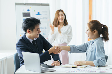 Group of beautiful designers in casual clothes is discussing affairs and smiling while working in studio. Two of them are shaking their hands