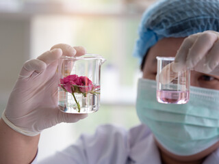 selective focus, two small beakers in scientist's hand, one with flower and the other with essencial