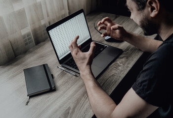 A man emotionally works with numbers at home on a laptop. Freelance businessman. The shareholder monitors the stock exchange. Accountant. Programmer, engineer. Angry and waving his hands. High quality