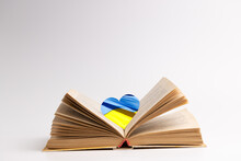 Open Book With Heart Symbol Colored Ukrainian Flag Over Grey Background. Copy Space. Side View. Concept
