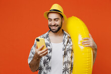 Young Smiling Happy Tourist Man In Beach Shirt Hat Hold Inflatable Ring Hold In Hand Use Mobile Cell Phone Isolated On Plain Orange Background Studio Portrait Summer Vacation Sea Rest Sun Tan Concept